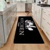 A black non-slip flannel area rug with white cutlery designs placed on a light wood floor in a kitchen.