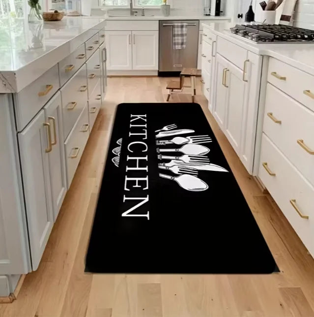 A black non-slip flannel area rug with white cutlery designs placed on a light wood floor in a kitchen.