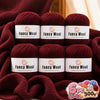 A set of six skeins of deep burgundy Fancy Wool yarn with yellow accents displayed on a red knitted fabric.