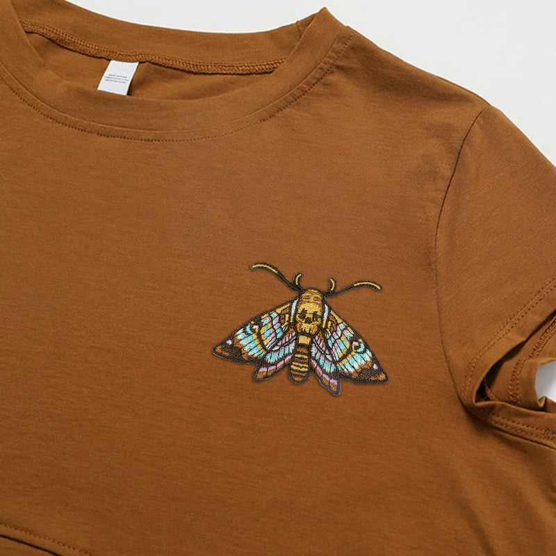 A brown t-shirt featuring an embroidered patch of a colorful moth on the chest.
