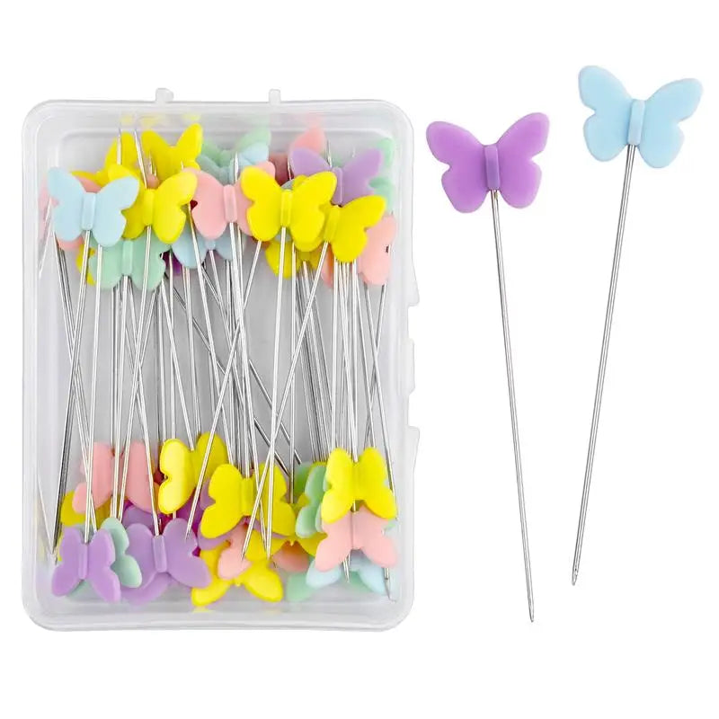 A clear plastic box containing dressmaking pins with colorful butterfly heads in purple and light blue.