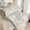 A rolled pastoral print lightweight summer quilt blanket with floral patterns resting on a white surface.