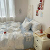 A bedroom featuring a bed with blue floral duvet covers and pillows, next to a white dresser.