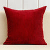 A deep red corduroy striped throw pillow cover resting on a light-colored sofa.