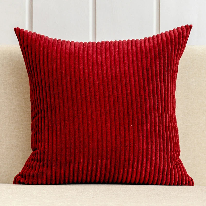 A deep red corduroy striped throw pillow cover resting on a light-colored sofa.