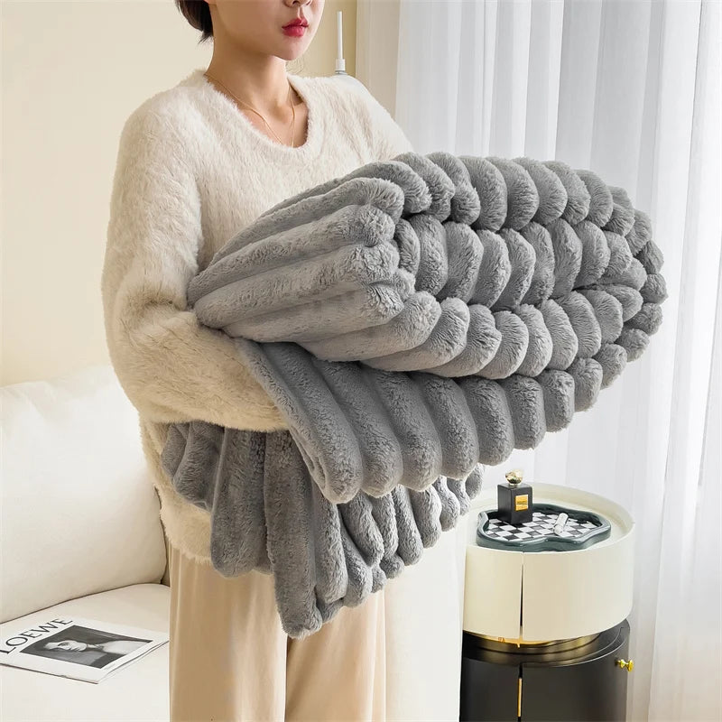 A woman is holding a large, fluffy gray plush winter blanket in front of a white window.