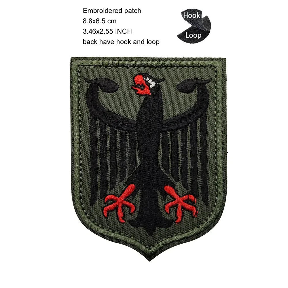 A dark olive green embroidered patch featuring a black eagle design on a fabric background.