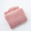 A pink knitted tassel throw blanket with a textured surface and fringed edge.