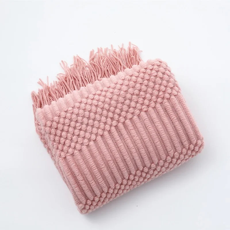 A pink knitted tassel throw blanket with a textured surface and fringed edge.