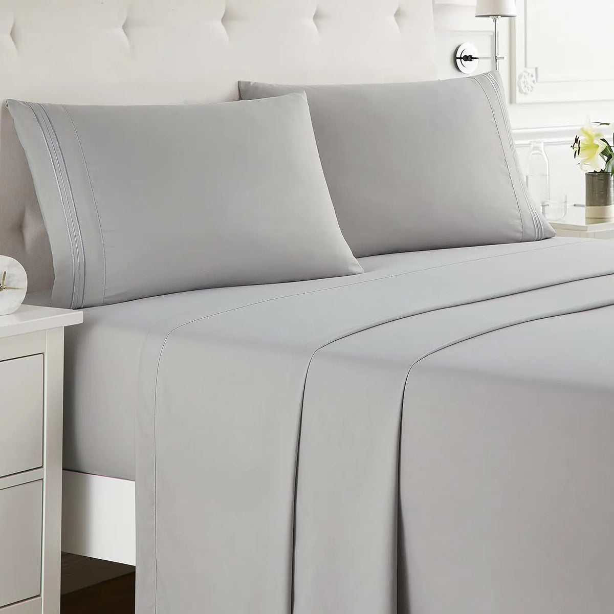 A set of gray microfiber bed sheets and pillows on a bed with a tufted headboard.