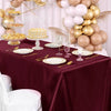 A maroon satin tablecloth set for elegant dining featuring gold and blush balloons and desserts