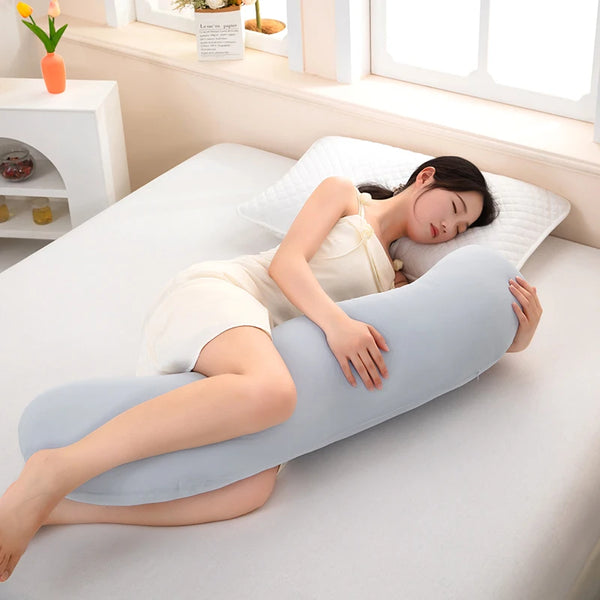 A woman lies on a white bed using a light blue ergonomic double wave curve pillow for support.