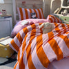 A pink and orange striped duvet cover set with a small stuffed animal on a bed.
