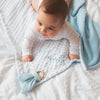 A baby is lying on a white blanket with the name James embroidered on it, surrounded by soft blue fabric.