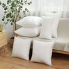 A collection of white cotton-filled decorative throw pillows arranged on a light-colored sofa near a window.