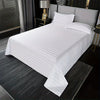 White luxury striped cotton flat sheet bedding on a bed with gray linens and dark wood accents.