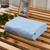 A light blue bamboo fiber cooling blanket is neatly folded on a wooden surface next to a framed picture.