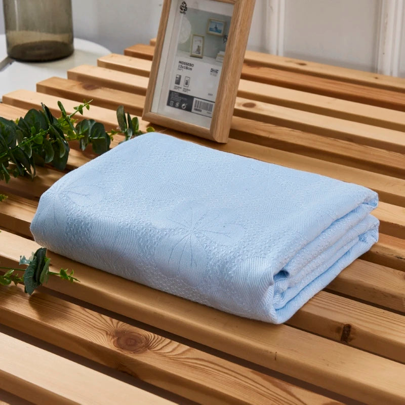 A light blue bamboo fiber cooling blanket is neatly folded on a wooden surface next to a framed picture.