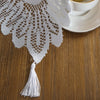 White retro lace table runner with tassels draped over a wooden table next to a cup.