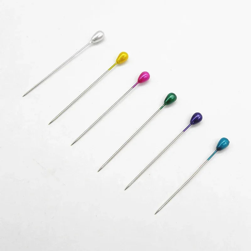 A collection of silver and colored pearl teardrop boutonniere pins for crafting.