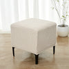 A beige geometric jacquard ottoman slipcover resting on a wooden floor near a window.