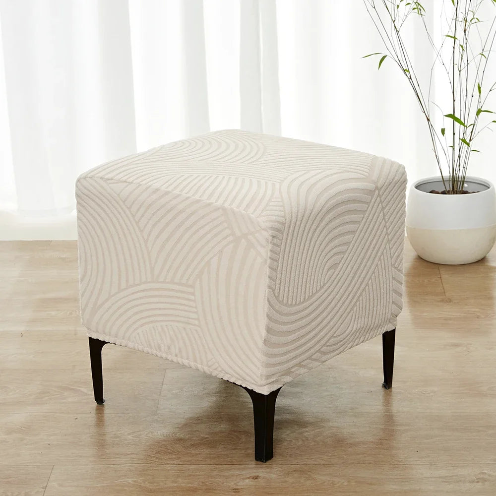A beige geometric jacquard ottoman slipcover resting on a wooden floor near a window.