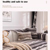 A plush velvet sofa protector cover in shades of gray and beige draped over a white sofa.