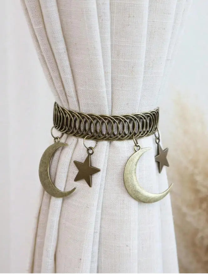 A vintage star and moon metal curtain clip featuring a coiled bar with crescent moon and star charms.