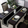 A dark wood dining table set with black placemats and white tableware, featuring geometric patterns.