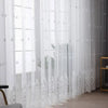 White embroidered floral tulle window curtain hanging in a window frame