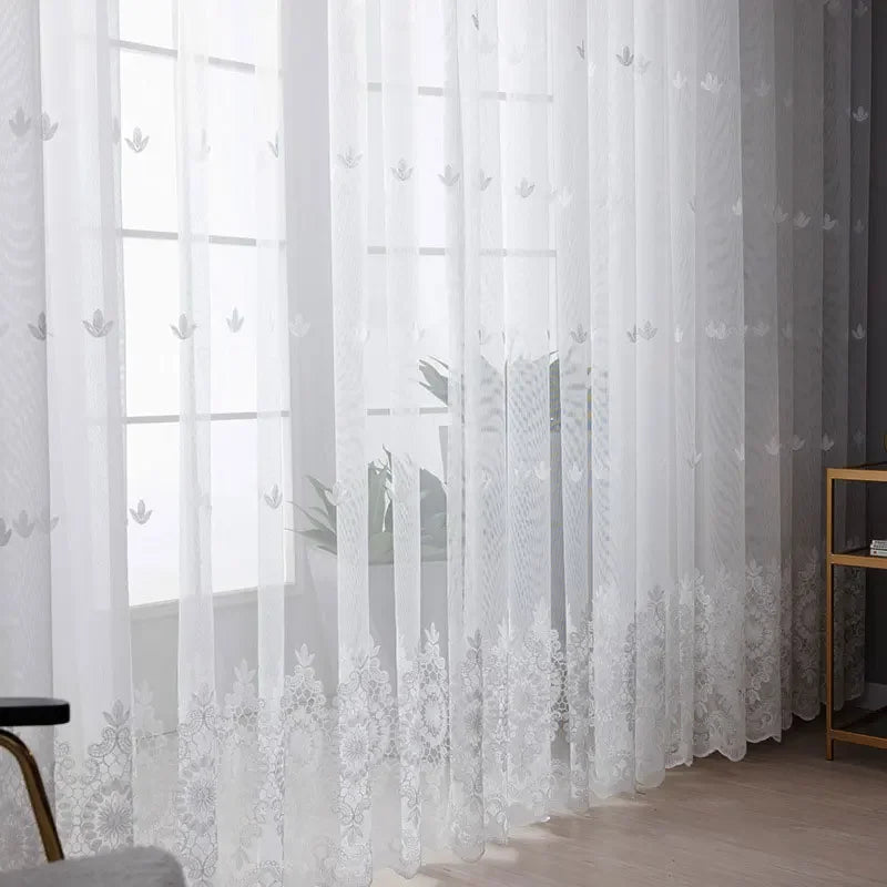 White embroidered floral tulle window curtain hanging in a window frame