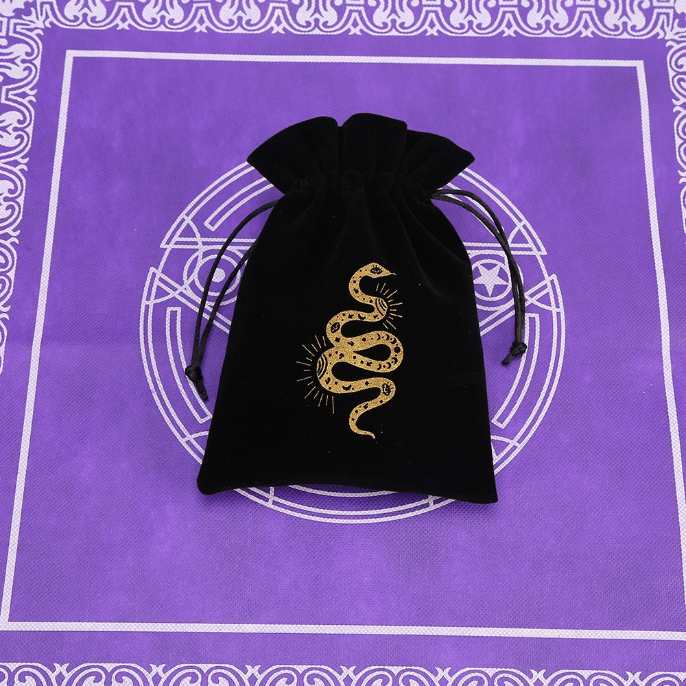 A black velvet tarot cards storage pouch with a gold coiled snake design rests on a purple patterned surface.