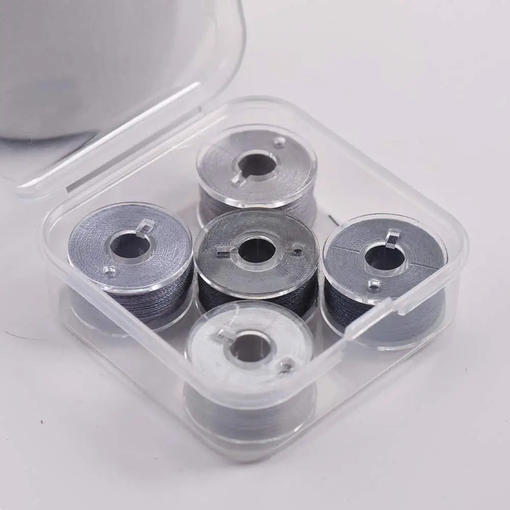 A clear plastic container holds several spools of prewound sewing machine bobbin threads.