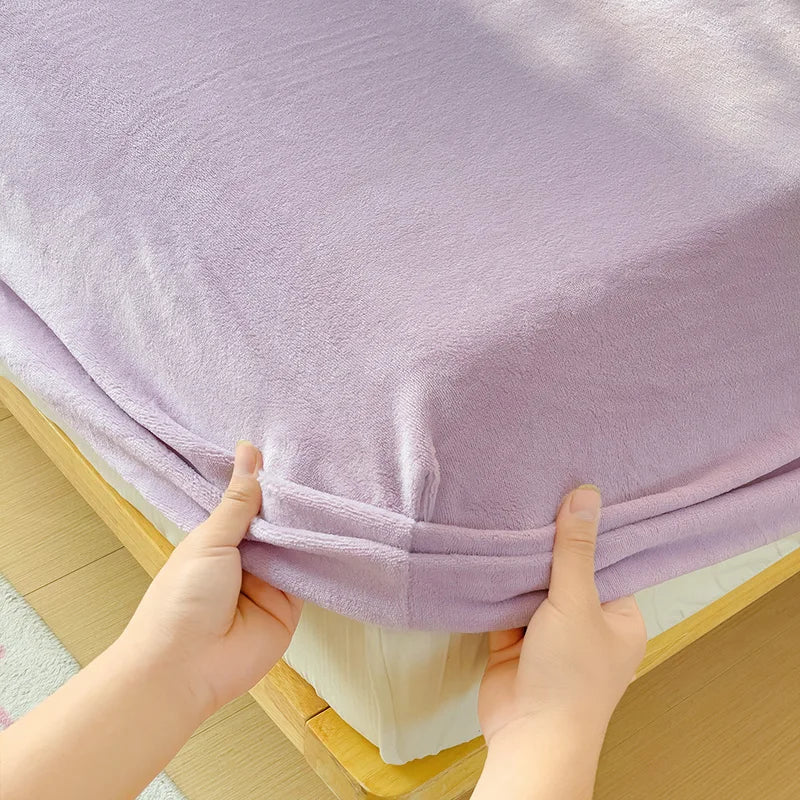 A hand is holding up a purple flannel fitted sheet with deep pockets, showing the fabric texture and elastic edge.