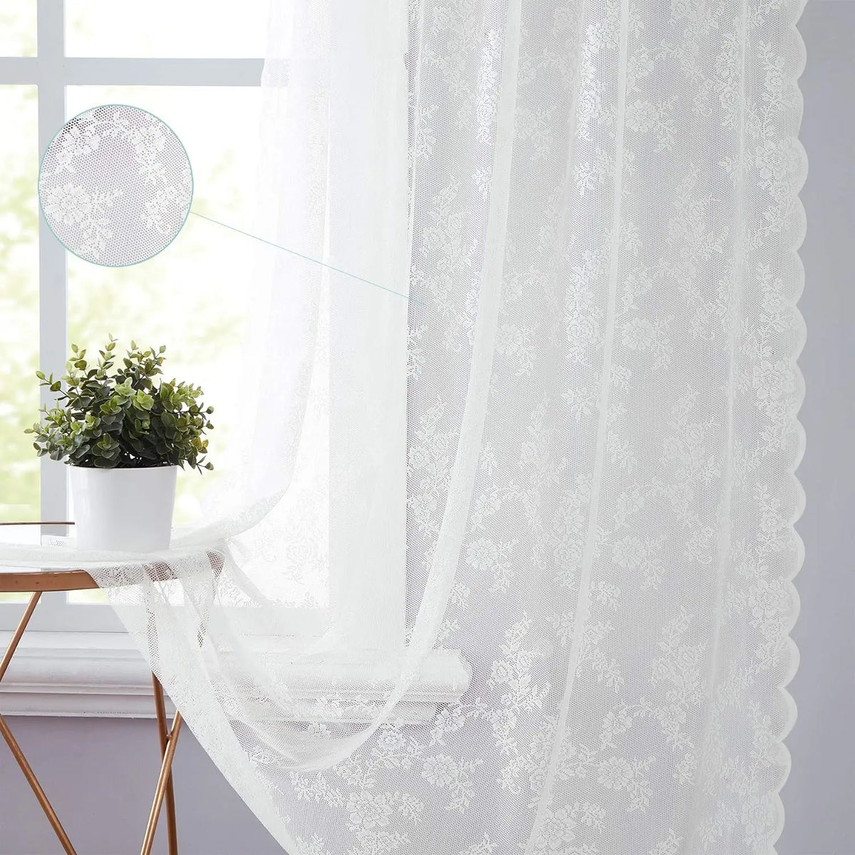 A sheer white floral lace curtain panel hangs in a bright window setting.
