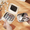 A hand opens a white magnetic sewing kit containing various specialty needles and thread on a wooden table.