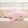 A pink giant shark plush toy lying on a light-colored surface near a window.