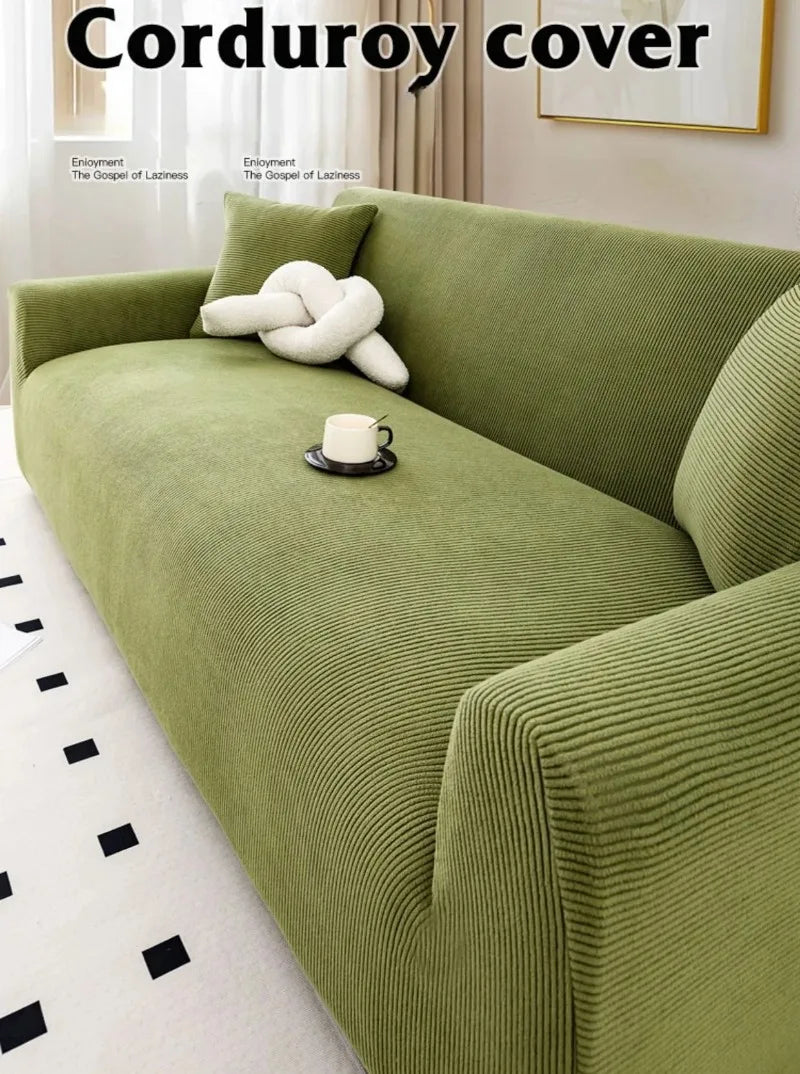 A moss green stretch jacquard sofa slipcover in a textured ribbed fabric with a white decorative pillow and a cup on the seat