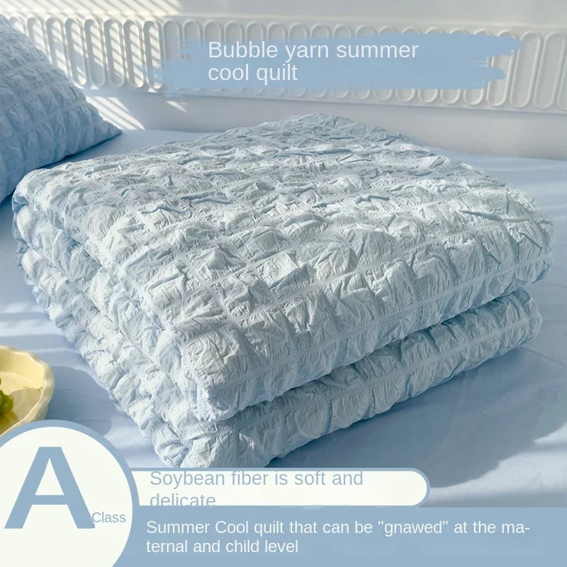 A stack of light blue bubble yarn summer cool quilt with a label indicating it is a Class A product.