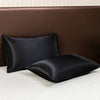 Black satin flat bed sheet set resting on a brown upholstered headboard.