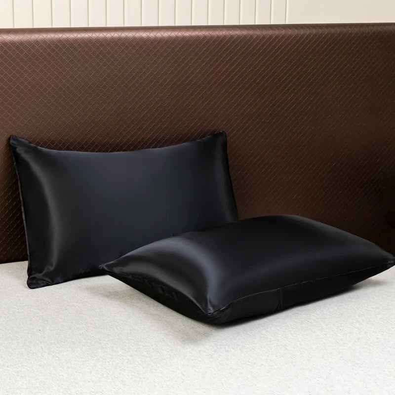 Black satin flat bed sheet set resting on a brown upholstered headboard.