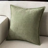 A square olive green chenille throw pillow resting on a light beige sofa.