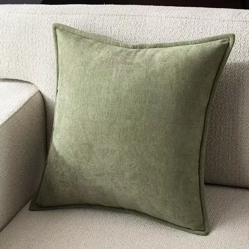 A square olive green chenille throw pillow resting on a light beige sofa.