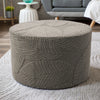 A round, textured gray ottoman footrest slipcover resting on a light gray rug.