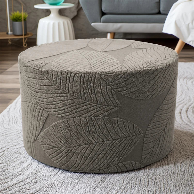 A round, textured gray ottoman footrest slipcover resting on a light gray rug.