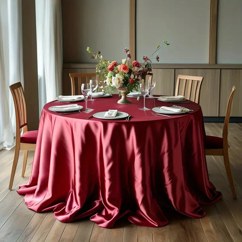A round table set for an event with a deep red satin overlay, white plates, and floral centerpieces.