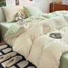 A close-up of a bed with light green and cream bedding, featuring pillows and a decorative silver wreath.