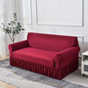 A deep red dustproof stretch sofa slipcover with a ruffled hem resting on a gray rug.
