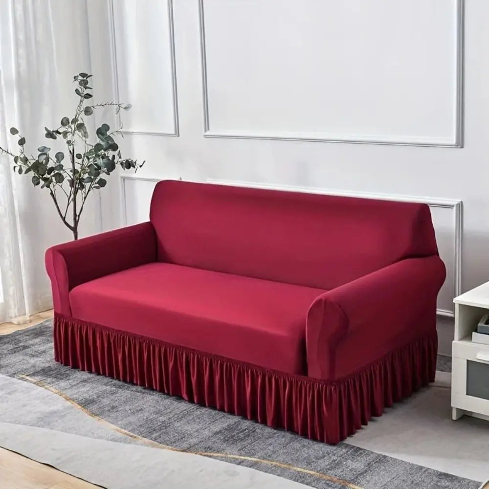 A deep red dustproof stretch sofa slipcover with a ruffled hem resting on a gray rug.