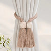 Hand-woven wooden curtain tiebacks in beige with tasseled ends tied to a white fabric drape.